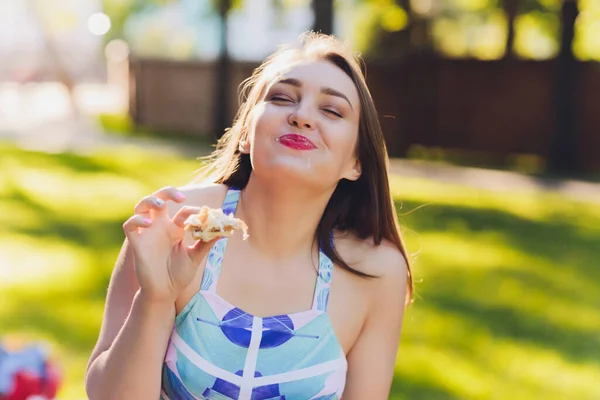 Lachende vrouw met een ontspannende lunchpauze buiten, ze zit op het gras en eet. — Stockfoto