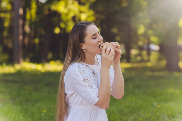 Lachende vrouw met een ontspannende lunchpauze buiten, ze zit op het gras en eet. — Stockfoto