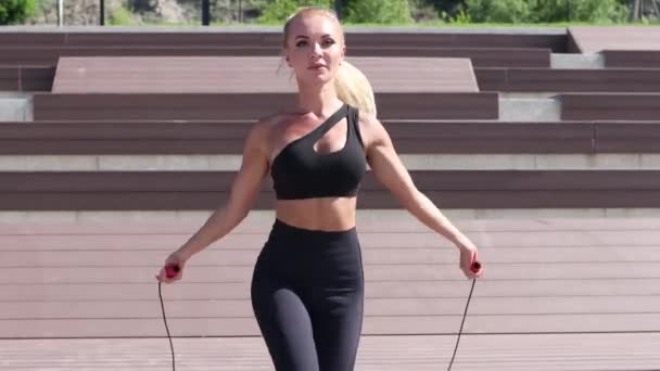 Ung sportig kvinna som har motion på strandpromenaden nära solsängen med hopprep. — Stockvideo