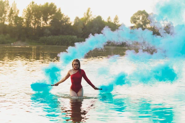 Belle jeune femme en maillot rouge posant près de la rivière. Style de vie estival. bombe fumigène — Photo