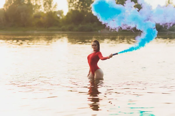 Bella giovane donna in costume da bagno rosso posa vicino al fiume. Stile di vita estivo. fumogeno — Foto Stock