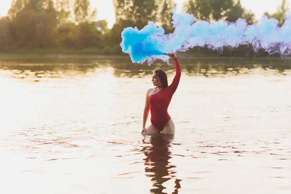 Hermosa joven en traje de baño rojo posando cerca del río. Estilo de vida. bomba de humo — Foto de Stock