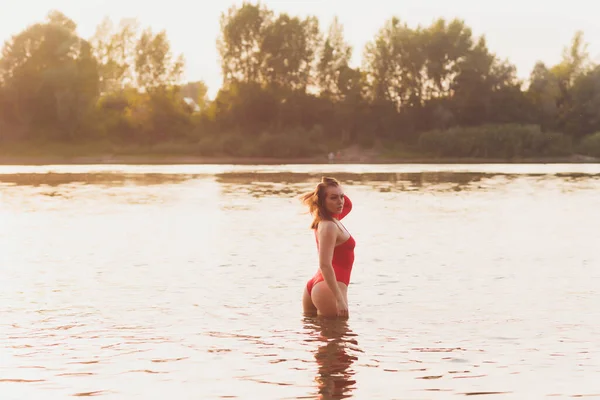 Piękna młoda kobieta w czerwonym stroju kąpielowym, pozująca w pobliżu rzeki. Letni styl życia. — Zdjęcie stockowe