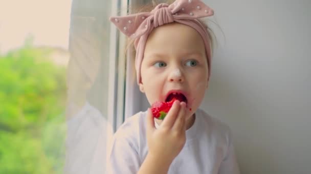 Счастливая девочка ест клубнику на летней домашней кухне. — стоковое видео