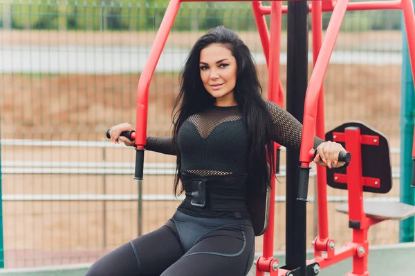 Mujer sonriendo mientras hace ejercicio en la parte superior del cuerpo usando la máquina de pesas afuera. — Foto de Stock