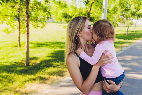 Mooie vrouw houdt een jaar oude baby in haar armen in het park. Moederschap en familie. Zorg en ontwikkeling van het kind. — Stockfoto