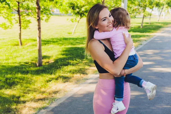 Mooie vrouw houdt een jaar oude baby in haar armen in het park. Moederschap en familie. Zorg en ontwikkeling van het kind. — Stockfoto