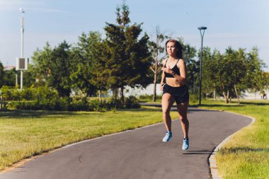 Genç bir kadın yazın parkta koşuyor..