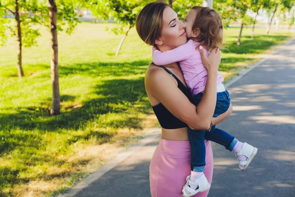 Mooie vrouw houdt een jaar oude baby in haar armen in het park. Moederschap en familie. Zorg en ontwikkeling van het kind. — Stockfoto