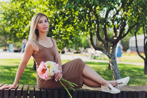 魅力的な女性は牡丹の花の花束を座って. — ストック写真