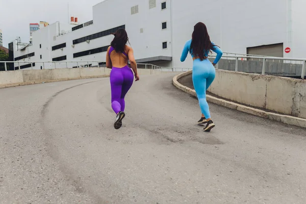 Två kvinnliga idrottare träning racing kör på övervåningen på stadstrappor i urban torv bakgrund. — Stockfoto