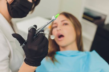 Diş hekimi hastasının dişlerini muayene ediyor..