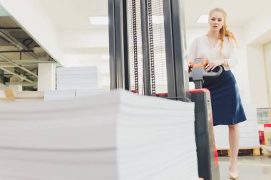Fabrika işçisi malları yüklemek için elektrikli çatal kaldırma kullanıyor. Genç kadın.