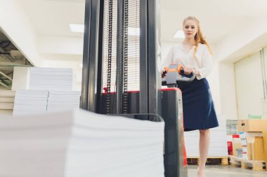 Fabrika işçisi malları yüklemek için elektrikli çatal kaldırma kullanıyor. Genç kadın.