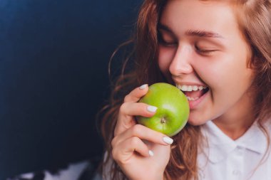 Güzel beyaz dişleri olan güzel genç bir kadın elinde bir elma tutuyor..