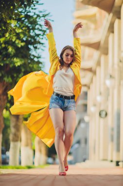 Moda eğilimleri gösteriyor. Koyu saçlı, çekici bir kadın, parlak sarı tüylü pelerinli..