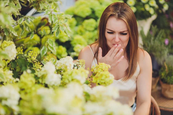 Young woman holds a lilac pinched her nose with fingers, allergic to flowers.