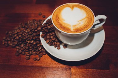 Arka planda kahve çekirdeği olan bir fincan kapuçino..