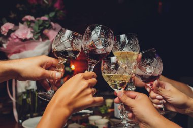 Bokeh arkaplanının önünde kadeh tokuşturup şampanya içen bir grup insanı yakından çek. Yaşlı insanların elleri.