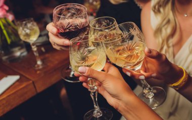 Bokeh arkaplanının önünde kadeh tokuşturup şampanya içen bir grup insanı yakından çek. Yaşlı insanların elleri.