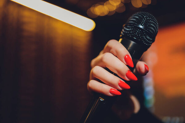 Microphone and female singer close up. Woman singing into a microphone, holding mic with hands.