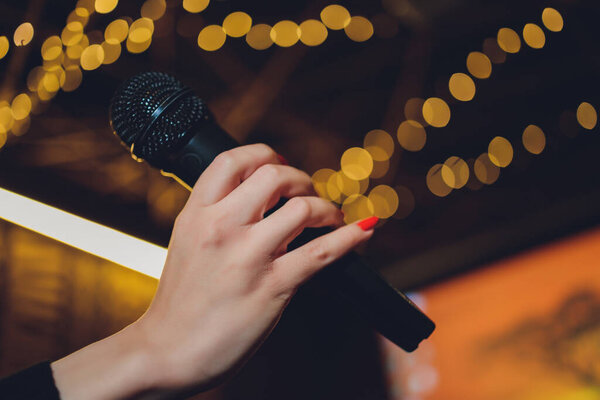 Microphone and female singer close up. Woman singing into a microphone, holding mic with hands.