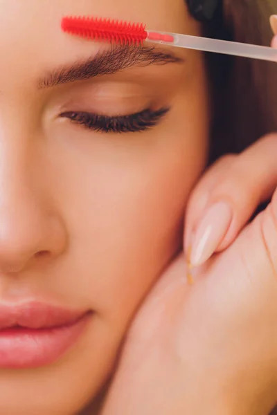 Young woman having professional eyebrow correction procedure in beauty salon.