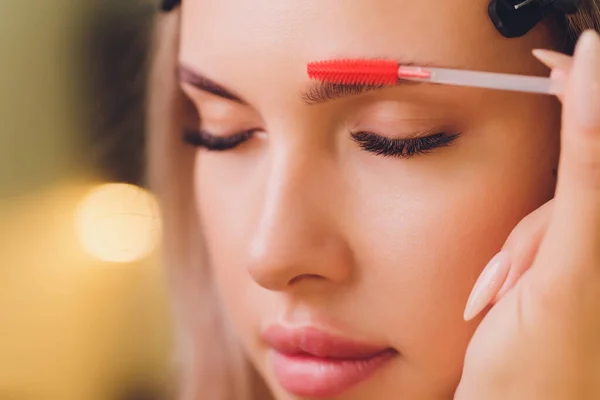 Young woman having professional eyebrow correction procedure in beauty salon.