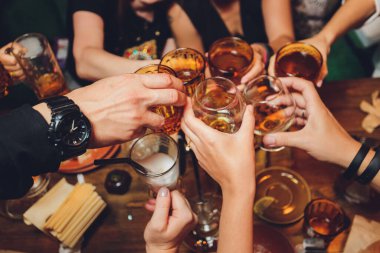 Bokeh arkaplanının önünde kadeh tokuşturup şampanya içen bir grup insanı yakından çek. Yaşlı insanların elleri.