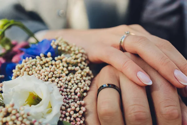 Vista de perto de recém-casados mãos segurando buquê de casamento colorido. Noiva e noivo a usar alianças de casamento. Fundo exterior. Conceito do dia do casamento. — Fotografia de Stock