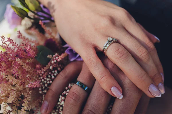 Närbild av nygifta händer som håller färgglada bröllop bukett. Brud och brudgum bär vigselringar. Bakgrund utomhus. Bröllopskoncept. — Stockfoto
