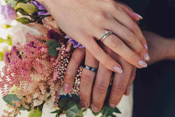 Vista de cerca de las manos de los recién casados que sostienen el colorido ramo de bodas. Novia y novio usando anillos de boda. Fondo exterior. Concepto día de boda. —  Fotos de Stock