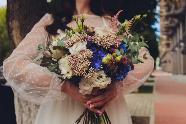 Krásná kytice různých barev v rukou nevěsty v bílých šatech. — Stock fotografie