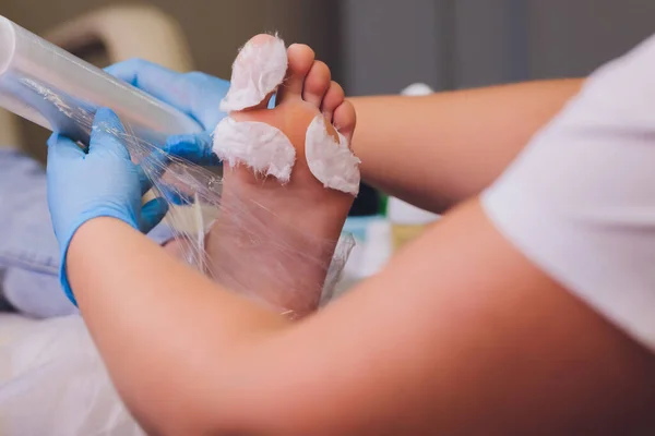 Le mani nei guanti si preoccupano delle unghie dei piedi. Salone di bellezza di pedicure. Crema idratante per piedi. — Foto Stock