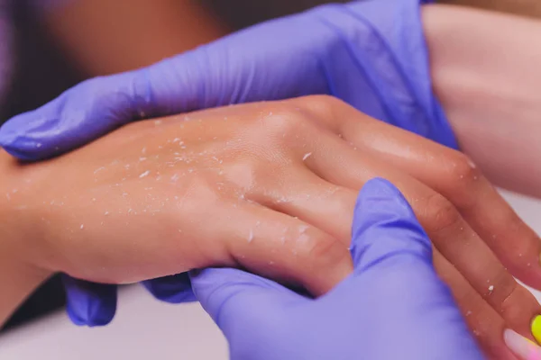 Esteticista o manicurista en guantes médicos especiales causa la crema en la mano de las mujeres. — Foto de Stock
