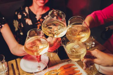 Bokeh arkaplanının önünde kadeh tokuşturup şampanya içen bir grup insanı yakından çek. Yaşlı insanların elleri.