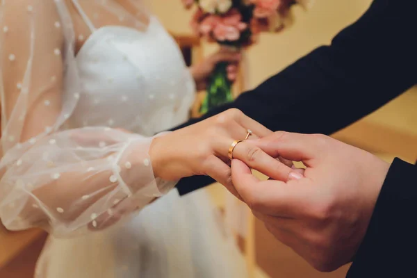 Os recém-casados trocam anéis, o noivo coloca o anel na mão das noivas no cartório do casamento.. — Fotografia de Stock