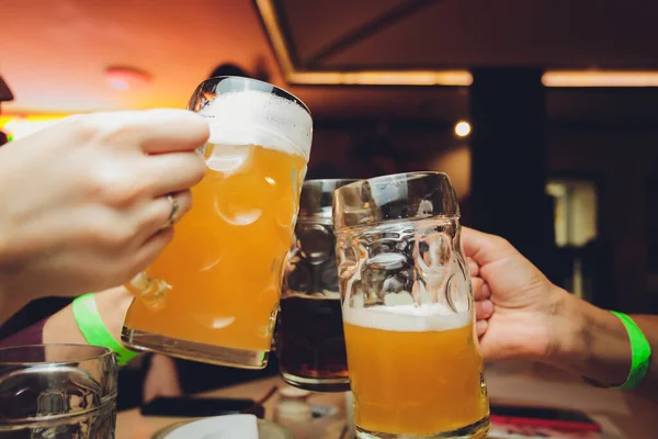 Nahaufnahme einer Gruppe von Menschen, die vor Bokeh-Hintergrund Gläser mit Bier klirren. Ältere Hände. — Stockfoto