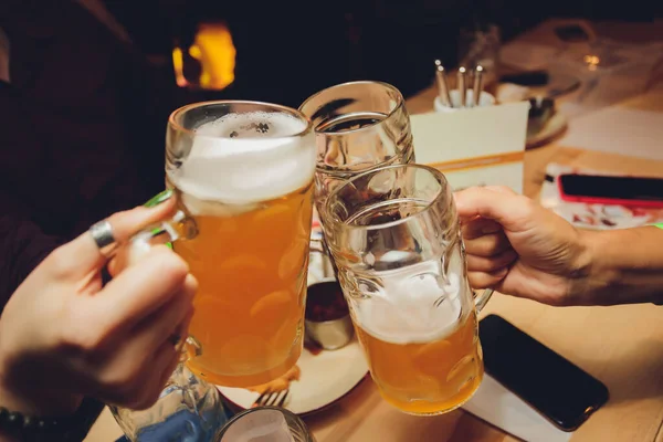 Nahaufnahme einer Gruppe von Menschen, die vor Bokeh-Hintergrund Gläser mit Bier klirren. Ältere Hände. — Stockfoto