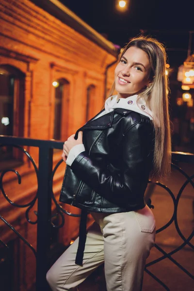 Junge schöne hübsche Frau lächelt und posiert auf der Straße der Stadt in der Nacht vor Abendlicht Bokeh Hintergrund. — Stockfoto