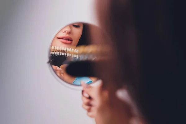 De tandarts vergelijkt patiënten tanden schaduw met monsters voor bleken behandeling. — Stockfoto