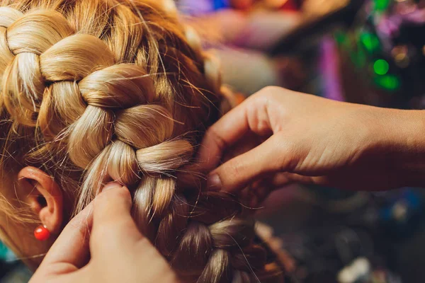 Processo de trançar o mestre tece tranças em sua cabeça menina loira no salão de beleza de perto. Cuidados com o cabelo profissional e criação de penteados. — Fotografia de Stock