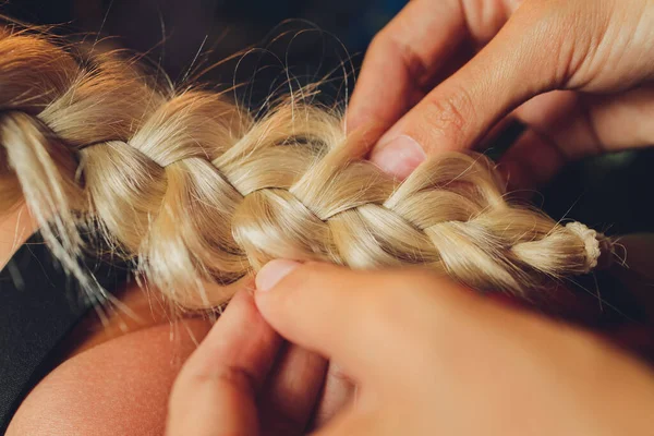 Processo de trançar o mestre tece tranças em sua cabeça menina loira no salão de beleza de perto. Cuidados com o cabelo profissional e criação de penteados. — Fotografia de Stock