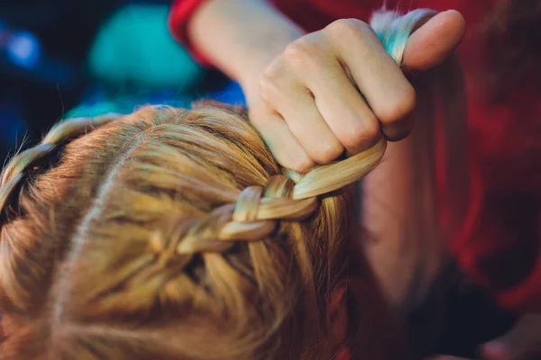 Processo de trançar o mestre tece tranças em sua cabeça menina loira no salão de beleza de perto. Cuidados com o cabelo profissional e criação de penteados. — Fotografia de Stock