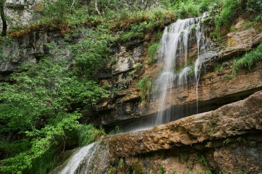 Uçurumdan büyük kaldırım taşları arasında küçük bir dağ nehri şelalesi manzarası.