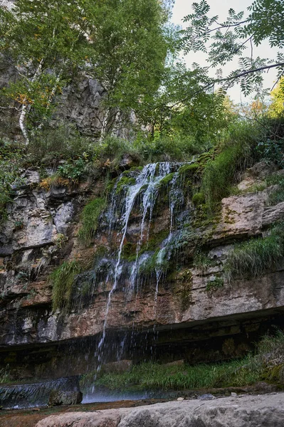 Vista de uma pequena cachoeira de rio de montanha entre grandes paralelepípedos de um penhasco. — Fotografia de Stock