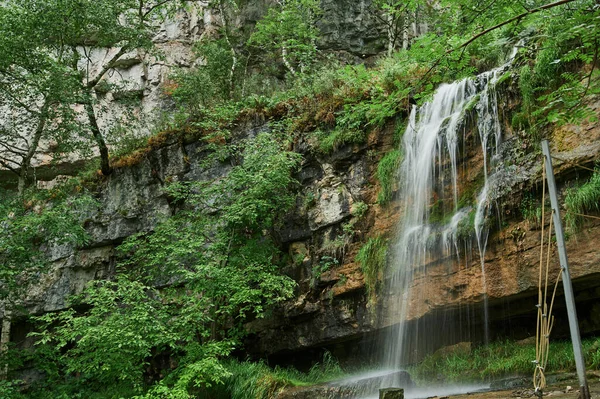 Zicht op een kleine berg rivier waterval tussen grote kasseien van een klif. — Stockfoto