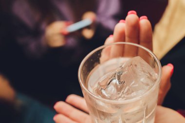 Dişi eller temiz bir bardak su tutuyor. Arka planda sümük gövdesi.