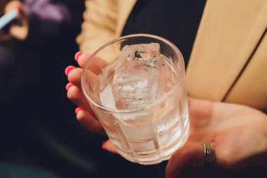 Dişi eller temiz bir bardak su tutuyor. Arka planda sümük gövdesi.