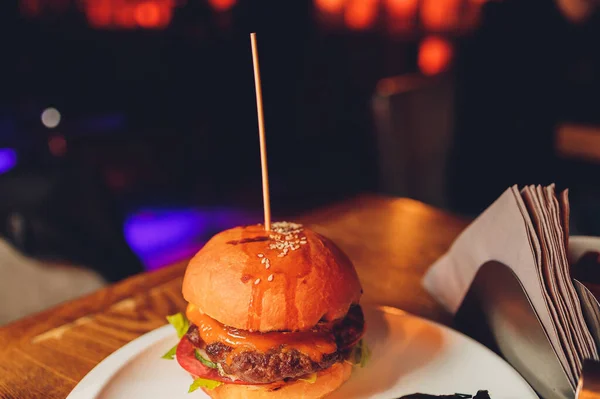 Gustoso hamburger di manzo grigliato con lattuga, ketchup, anelli di cipolla, peperoncino e maionese servito su pezzi di carta marrone su un rustico tavolo di legno del bancone, con copyspace. — Foto Stock